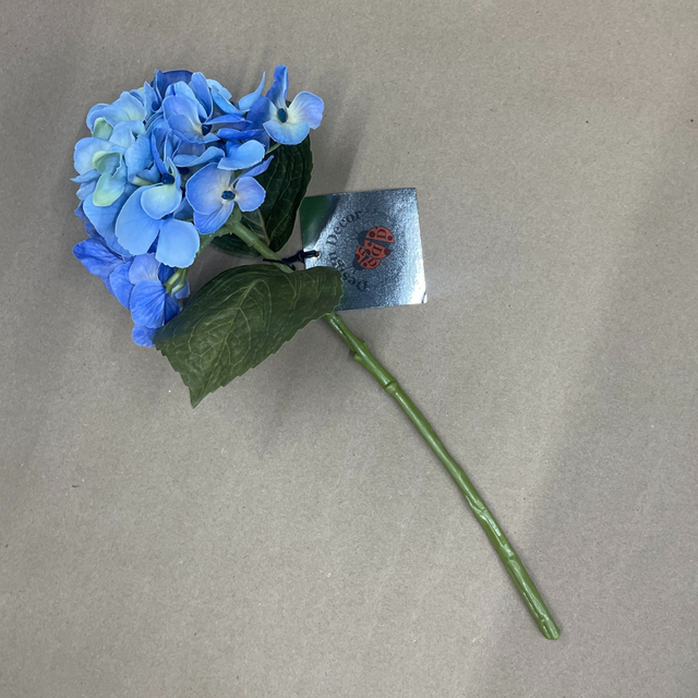 Artificial blue hydrangea flower with a green stem on a beige background