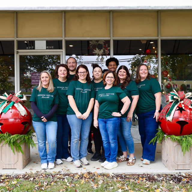 Group of people in matching green shirts standing in front of a store with Christmas decorations.