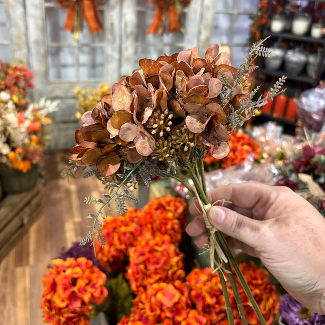 Hand holding a bouquet of pinecones and flowers with a festive background
