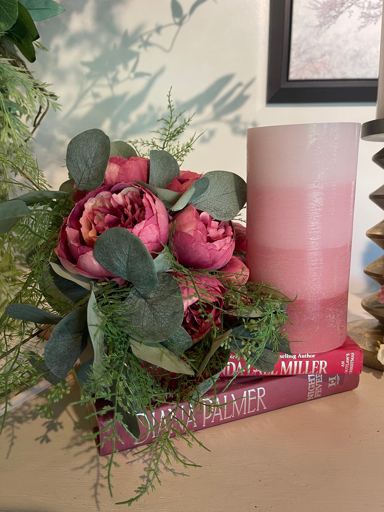 pink water fountain candle on stack of decorative books and beside a bundle of faux pink peonies