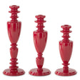 Three glossy red ceramic candlesticks in graduated sizes, arranged from tallest on the left to shortest on the right, set against a plain white background.