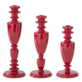Three glossy red ceramic candlesticks in graduated sizes, arranged from tallest on the left to shortest on the right, set against a plain white background.