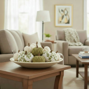 A small decorative pumpkin with a white fabric body and an olive green leaf pattern, featuring a natural brown stem, set against a plain white background.
