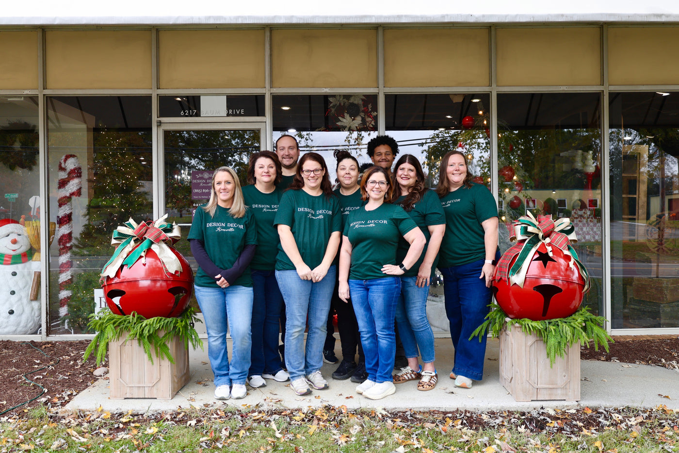 Group of people in matching green shirts standing in front of a store with Christmas decorations.