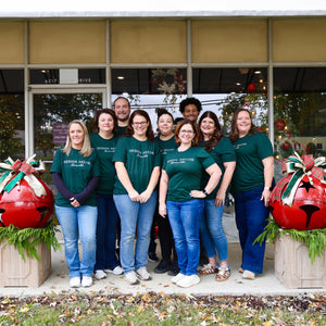 Group of people in matching green shirts standing in front of a store with Christmas decorations.