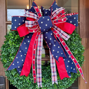 Green wreath with a large red, white, and blue bow on a wooden door.
