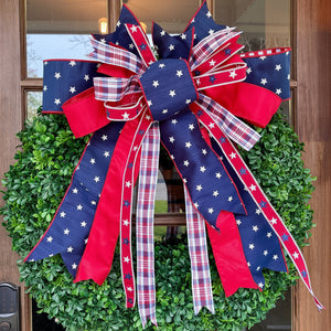 Green wreath with a large red, white, and blue bow on a wooden door.