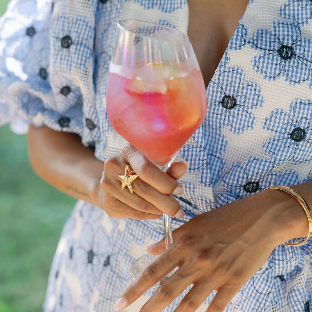 Person holding a pink cocktail in a floral dress with a blurred green background