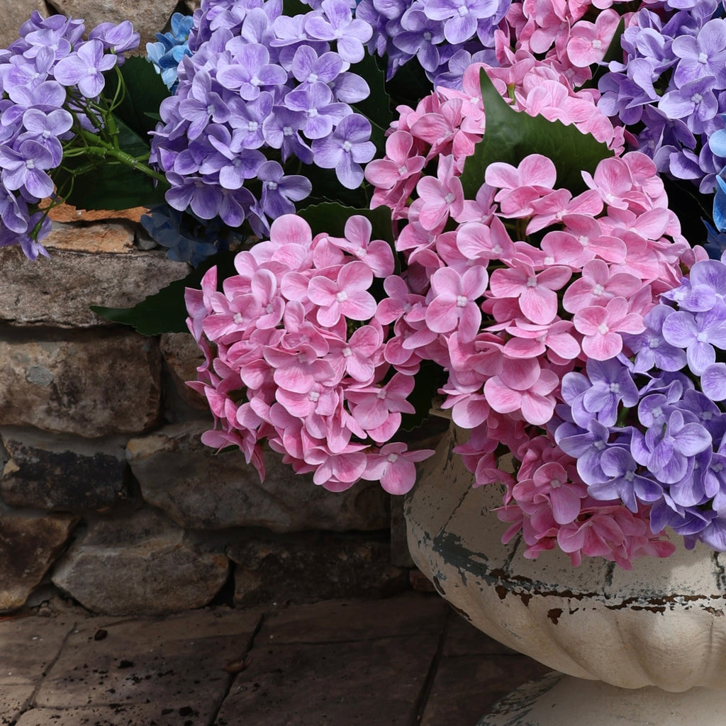 Multicolored flowers in a pot on a stone patio with a wooden wall and glass door in the background.