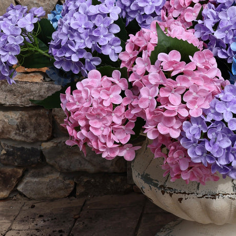 Multicolored flowers in a pot on a stone patio with a wooden wall and glass door in the background.