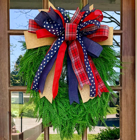Green wreath with a large red, white, and blue bow on a wooden door.