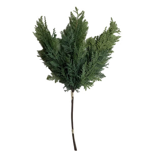 A single artificial green evergreen branch with dense textured foliage and a brown stem, photographed against a plain light gray background.