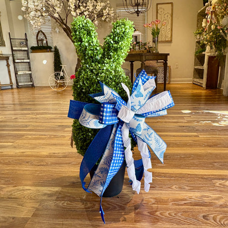 Decorative topiary with a large blue and white bow on a wooden floor.