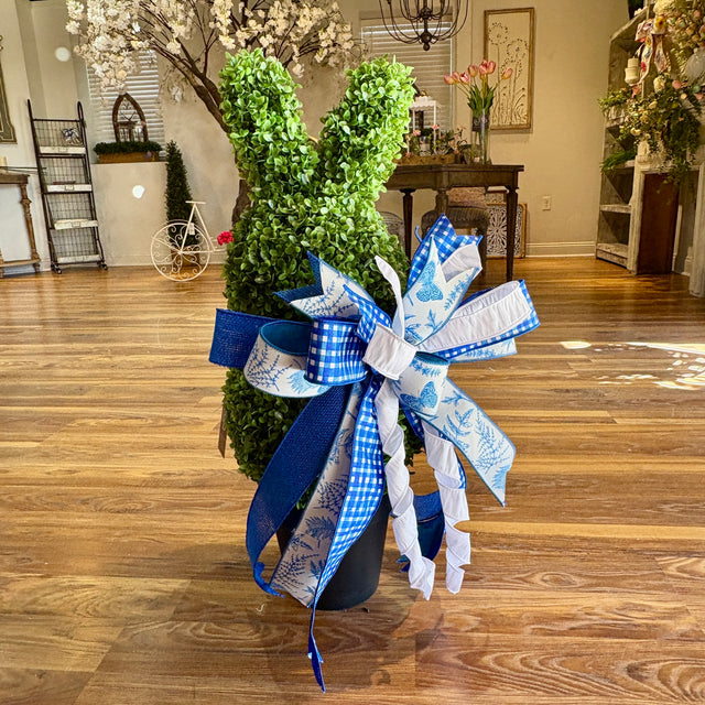 Decorative topiary with a large blue and white bow on a wooden floor.