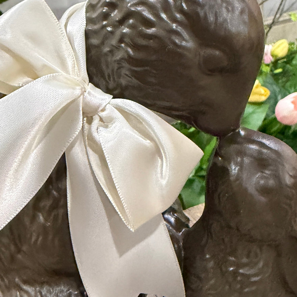 Faux chocolate sculpture of two kissing bunnies with a large white bow, set against a blurred floral background.