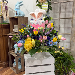 Decorative Easter display with flowers, a bunny, and a wooden crate in a room setting.