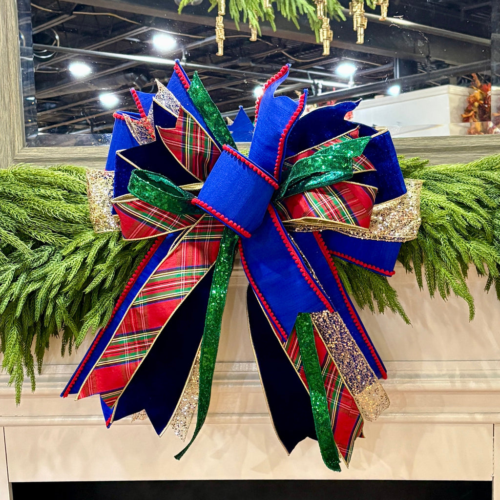 Decorative Christmas bow with red, green, and blue plaid patterns on a fireplace mantel.
