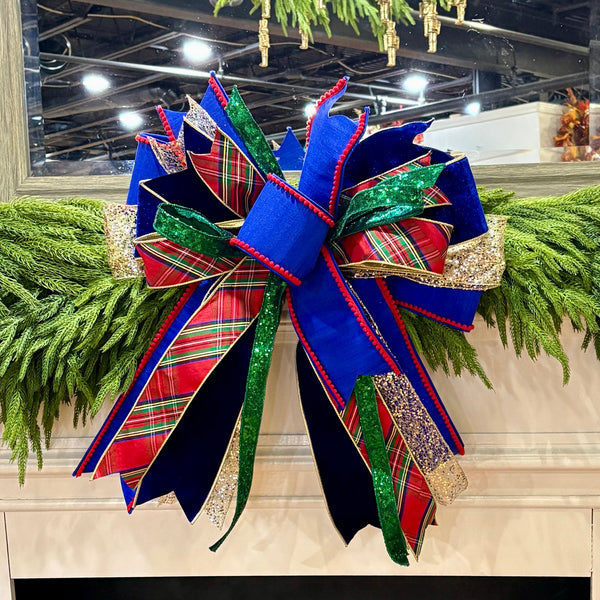 Decorative Christmas bow with red, green, and blue plaid patterns on a fireplace mantel.