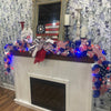 Decorative mantel with American flag-themed decorations and lights on a floral wallpapered wall.