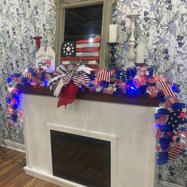 Decorative mantel with American flag-themed decorations and lights on a floral wallpapered wall.