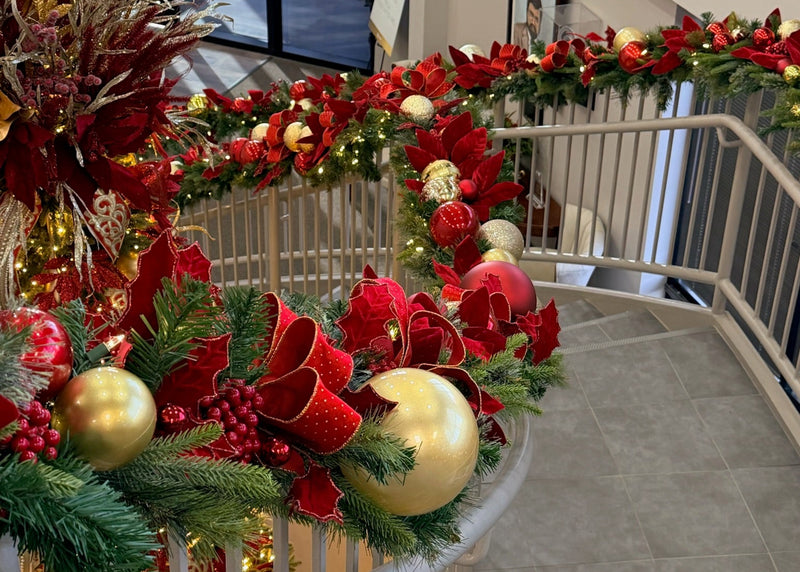 Decorative Christmas garland with red bows and gold ornaments on a staircase railing.