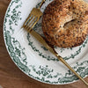 Bagel on a decorative plate with a gold fork on a wooden table