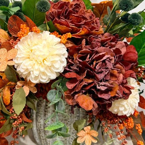An autumn-themed artificial floral arrangement in a textured gray ceramic pot, featuring burgundy and cream chrysanthemums, orange berries, eucalyptus, and fall leaves.