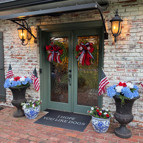Front door of a house with patriotic decorations including American flags, flowers, and a doormat.