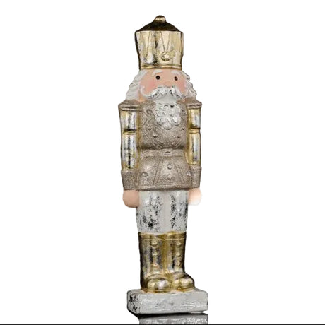 A vintage-style nutcracker figurine with a distressed silver and gold finish, featuring a pink face, white beard, and standing on a small base against a black background.