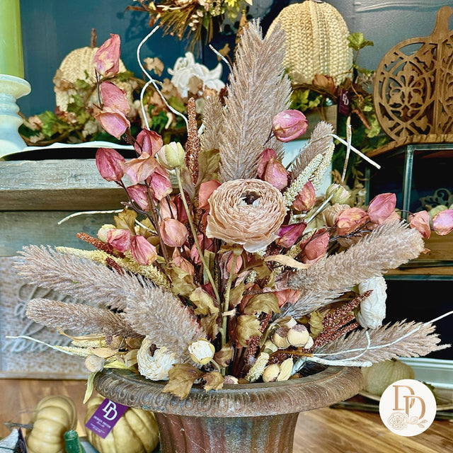 Decorative floral arrangement with pink flowers and pampas grass in a wooden vase on a table.