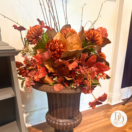 Decorative autumnal flower arrangement in a brown urn on a wooden floor.