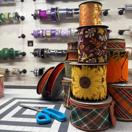 Colorful spools of fall wired ribbon with a pair of blue scissors on a grid-patterned surface.
