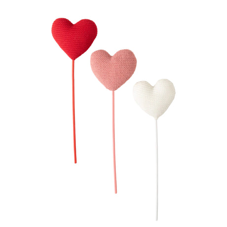 Three knit heart-shaped lollipops in red, pink, and white on a white background